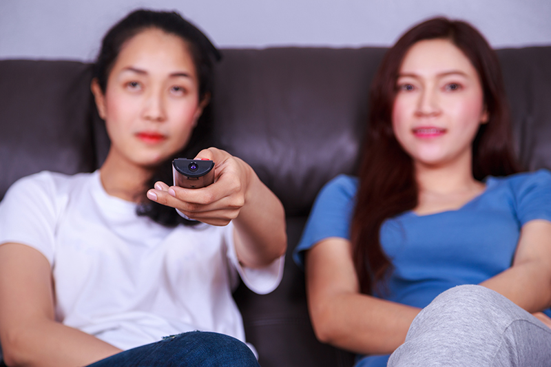 two best friends watching tv with remote on sofa in living room at home